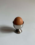 Stainless steel egg holder with a brown egg, featuring an elegant matte finish, perfect for kitchen decor and family breakfasts.