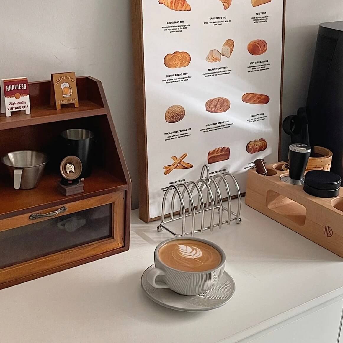 Stainless steel toast holder on a kitchen counter with coffee and bread chart in background.