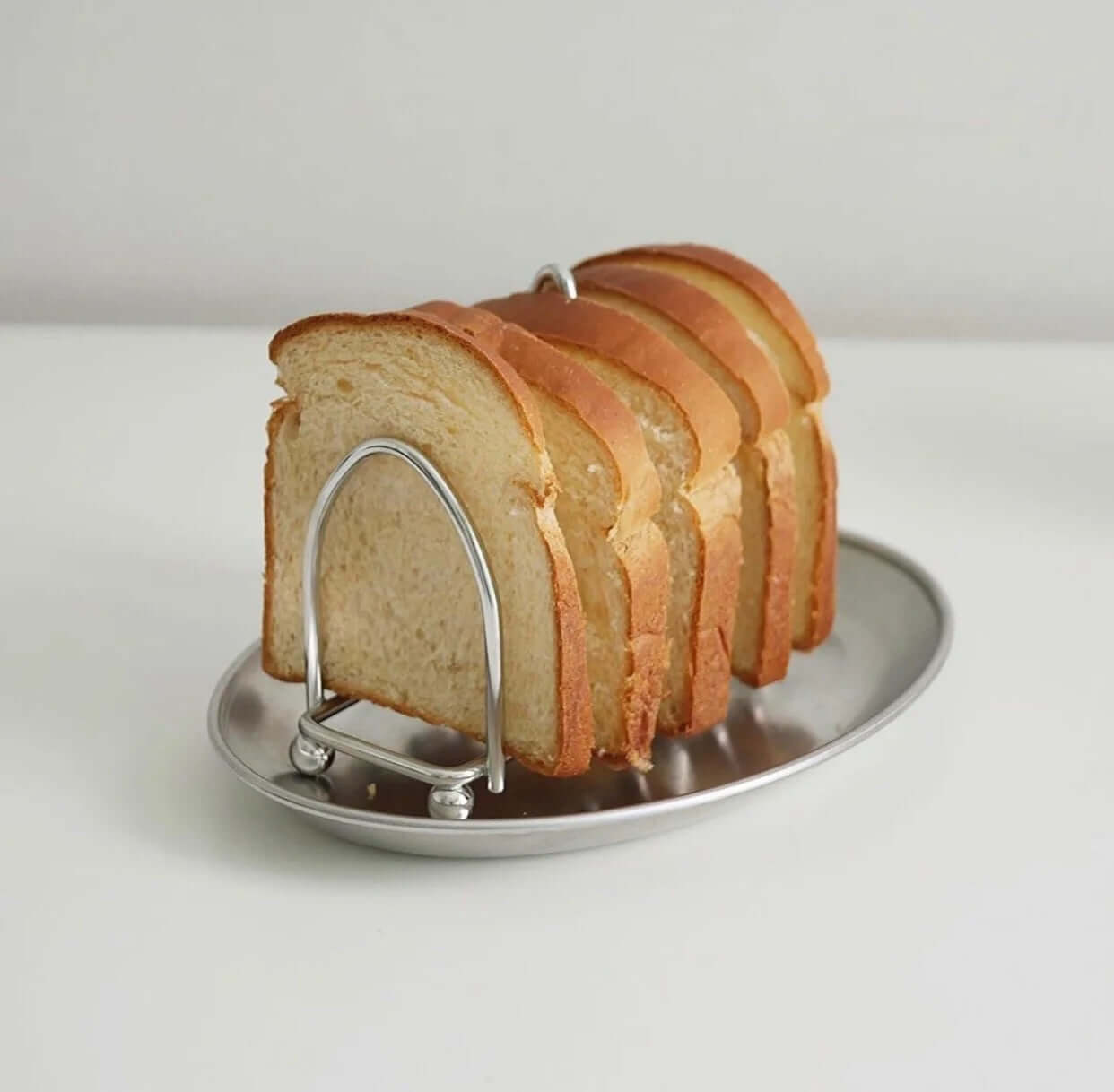 Stainless steel toast holder with six slices of bread, featuring a mirror finish for an elegant breakfast presentation.