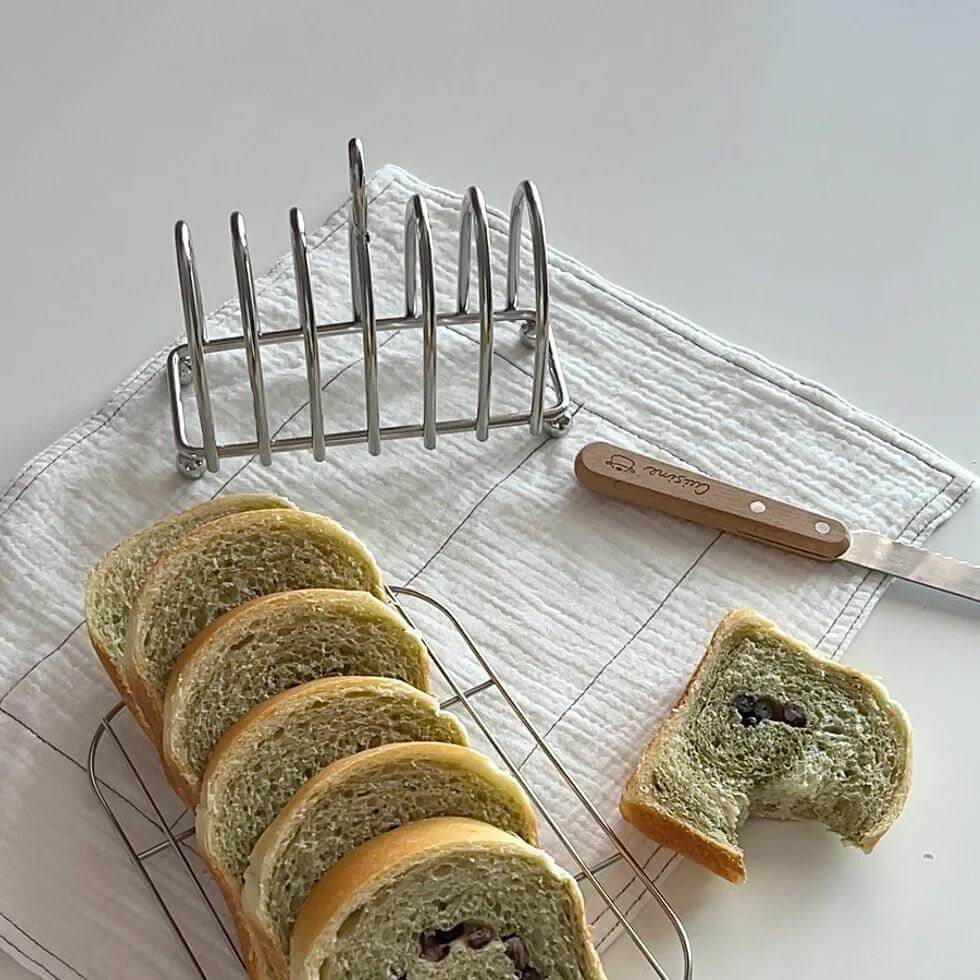 Elegant stainless steel toast holder with mirror finish, featuring six slices of bread on a table with a knife nearby.
