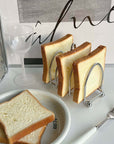 Stainless steel toast holder with six slices on a breakfast table, next to a white plate and fork, offering a stylish dining experience.