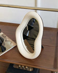 Nordic asymmetric cream mirror, 29x22 inches, on wooden surface. Stylish home decor with free shipping.