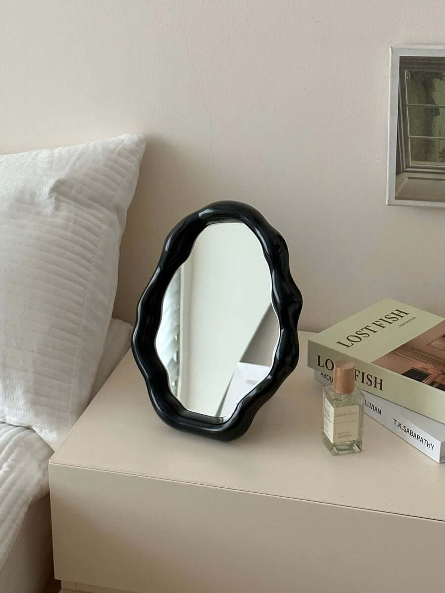 Nordic cloud-shaped vanity mirror in black, displayed on a table beside a bed and books, measuring 27x20cm for stylish decor.
