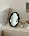 Nordic cloud-shaped vanity mirror in black, displayed on a table beside a bed and books, measuring 27x20cm for stylish decor.