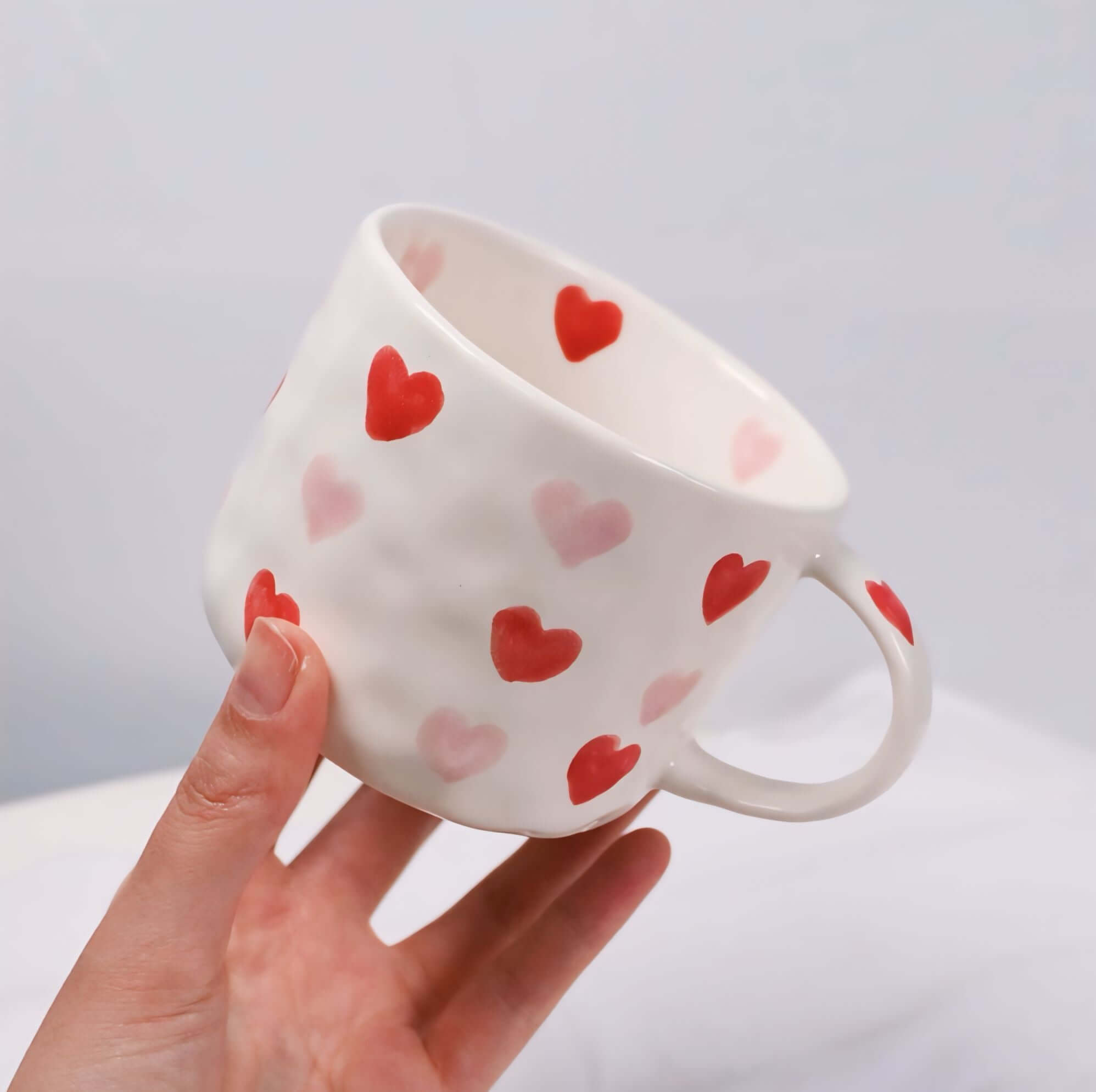 Hand-painted love coffee mug with red and pink hearts, beige ceramic design, 300ml capacity, held in hand.