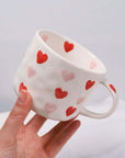 Hand-painted love coffee mug with red and pink hearts, beige ceramic design, 300ml capacity, held in hand.