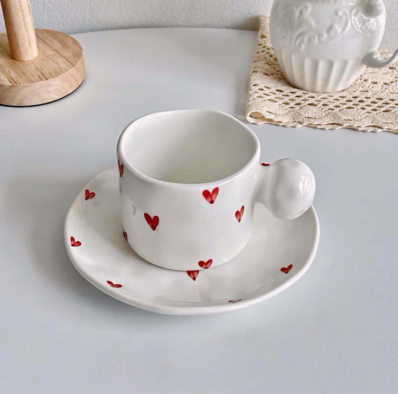 White ceramic mug and saucer set with red heart designs on a table.