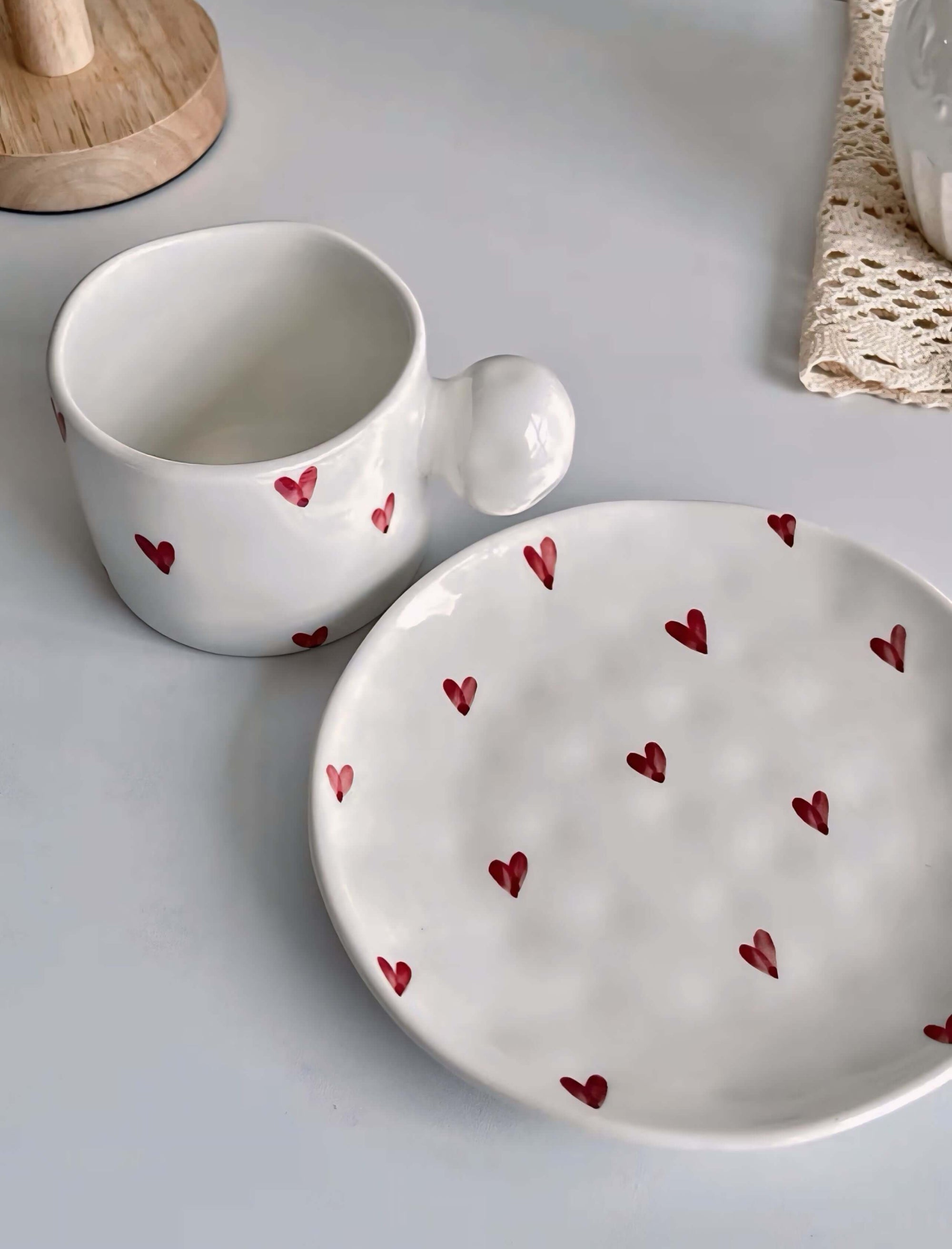 Ceramic mug and saucer set, decorated with red heart designs, featuring a 250ml capacity cup and matching plate on a white surface.