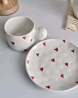 Ceramic mug and saucer set, decorated with red heart designs, featuring a 250ml capacity cup and matching plate on a white surface.