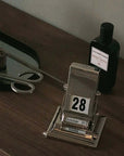 Timeless Rotating Desk Date Keeper on a wooden desk next to decor items, showcasing minimalist elegance and functionality.
