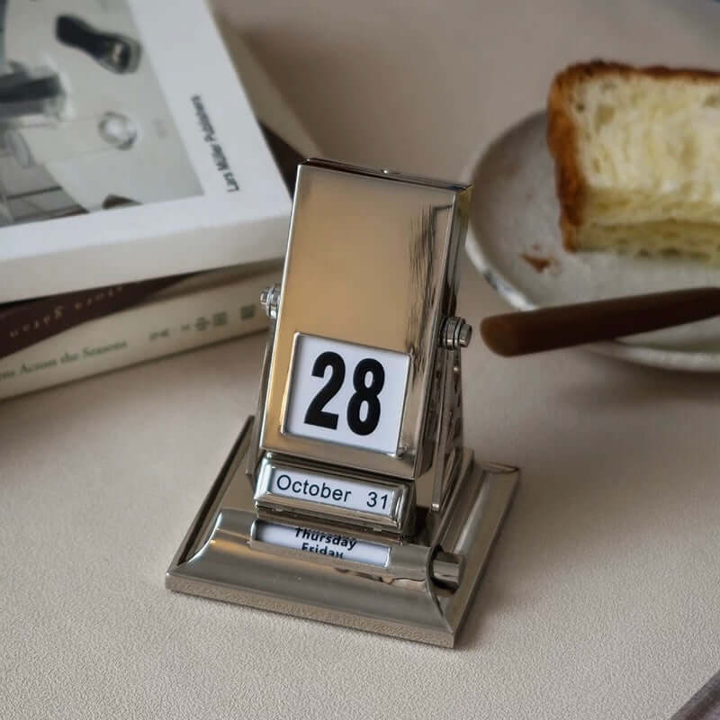 Elegant Nordic Rotating Desk Calendar with stainless steel finish, showcasing October 28th date, minimalist design on a desk.