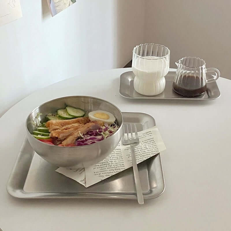 Stainless steel serving tray set with food and drink, showcasing urban chic minimalist design on a white table.
