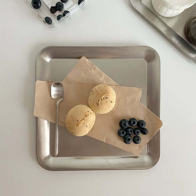Stainless steel serving tray with cookies, blueberries, and spoon, showcasing minimalist urban chic design.