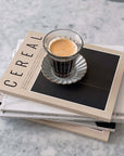 Zinc glass cup on Marumitsu Barbarie saucer, placed on stacked Cereal magazines on a marble table.