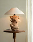Unique custom-crafted wooden lamp on a round table near a window, showcasing artistic design with a natural wood finish.