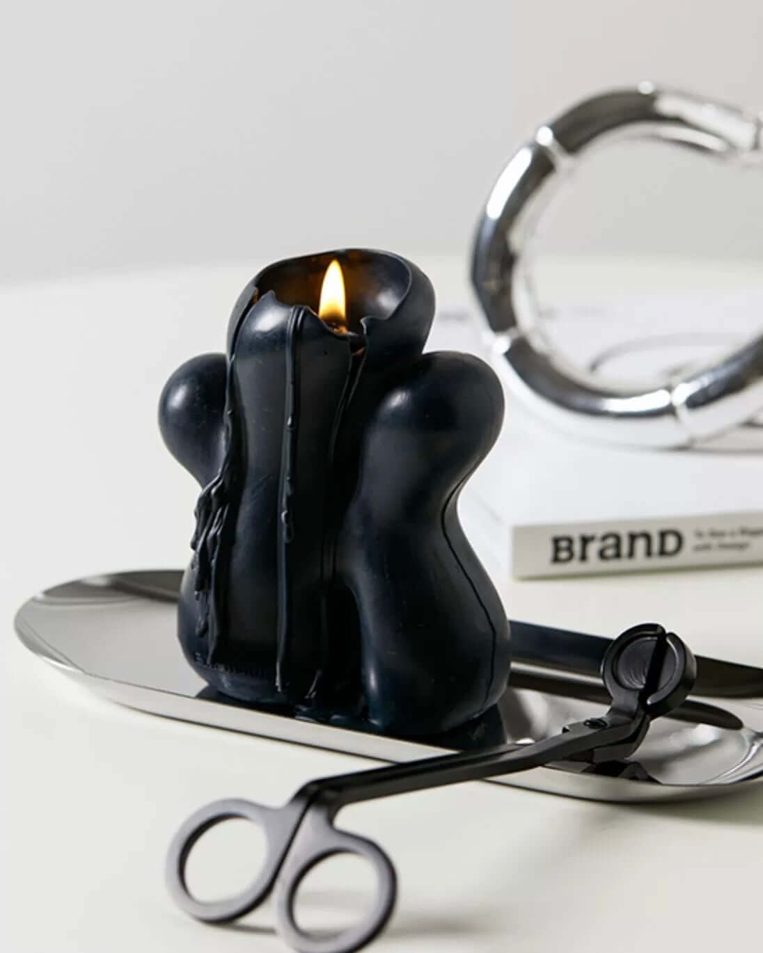 Black candle on stainless steel tray with wick trimmer, minimalist decor, modern home accessory display.