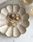 Elegant ceramic jewelry dish holding gold rings and pearl necklace, styled on a marble surface for chic aesthetic display.