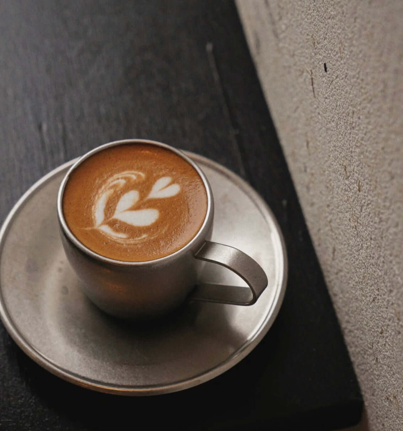 Vintage inox cup and saucer with latte art on a wooden table, made of 18-8 stainless steel from Japan.