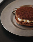 Stainless steel round plate with a chocolate dessert and fork on a dark table.
