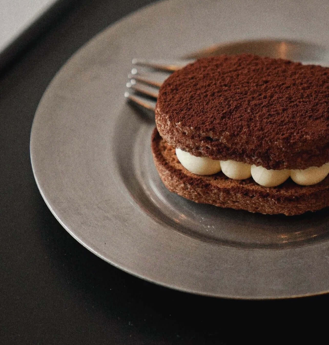 Stainless steel round plate with a chocolate dessert and fork on a dark table.