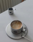 Stainless steel cup and saucer set with coffee, showcasing sleek design perfect for various occasions.