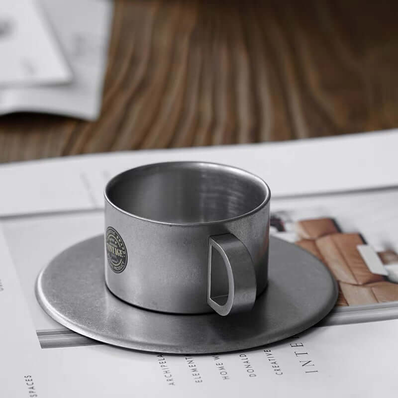 Vintage INOX stainless steel cup and saucer, 90ml, on a table. Durable, chic design for versatile use. Dishwasher safe, made in Japan.