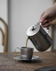 Stainless steel VINTAGE INOX cafe pot pouring coffee into a matching cup on a wooden table.