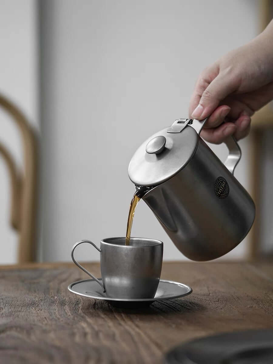 Stainless steel VINTAGE INOX cafe pot pouring coffee into a matching cup on a wooden table.