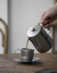 Stainless steel VINTAGE INOX cafe pot pouring coffee into a matching cup on a wooden table.