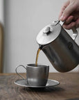 Pouring coffee from VINTAGE INOX stainless steel cafe pot into matching cup, showcasing durable and chic design. Made in Japan.