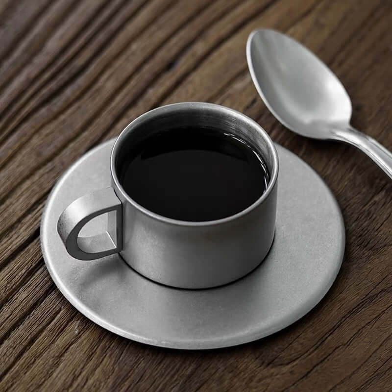 Stainless steel VINTAGE INOX cup and saucer on a wooden table, showcasing elegant design and durable materials.