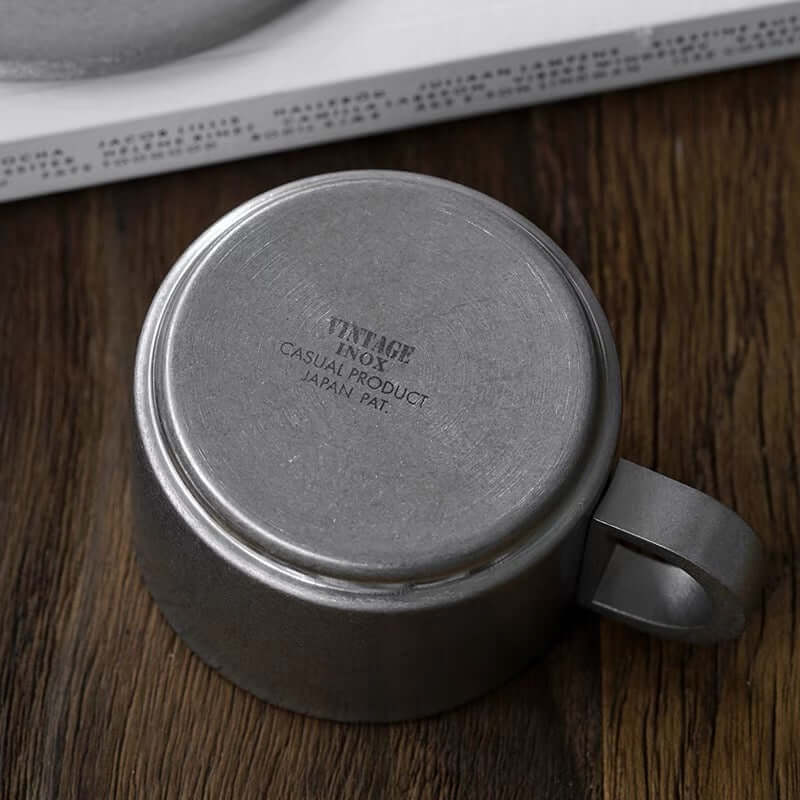 Vintage INOX stainless steel cup bottom view showing engraved details on wooden table.