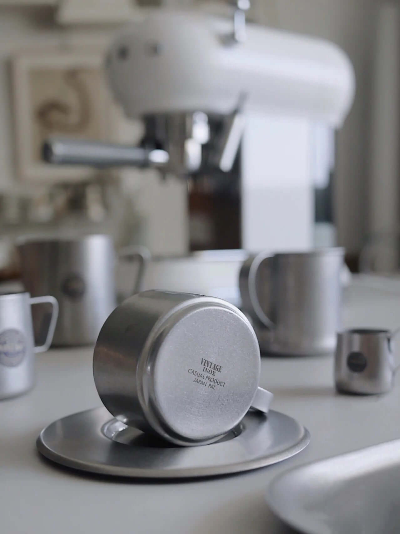 Vintage INOX stainless steel cup and saucer set on kitchen counter, showcasing durable and chic design with background kitchenware.