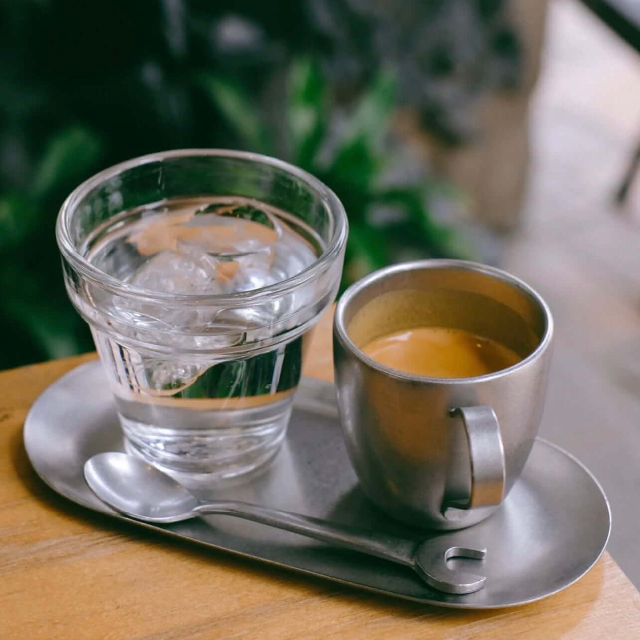 Vintage INOX stainless steel oval tray with coffee and glass of water on a wooden table.