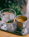 Vintage INOX stainless steel oval tray with coffee and glass of water on a wooden table.