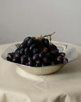 Sculpted Stainless Steel Bowl filled with black grapes on a linen tablecloth