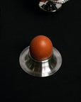 Stainless Steel Egg Cup with a flared base holding a brown egg on a black table
