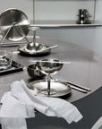 Set of Six Stainless Steel Plates stacked on a stand beside a dessert coupe on a black table