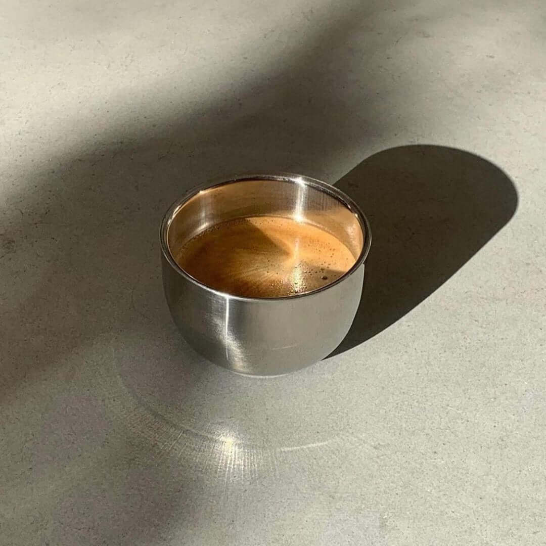 Stainless steel spherical cup with coffee on a sunlit surface