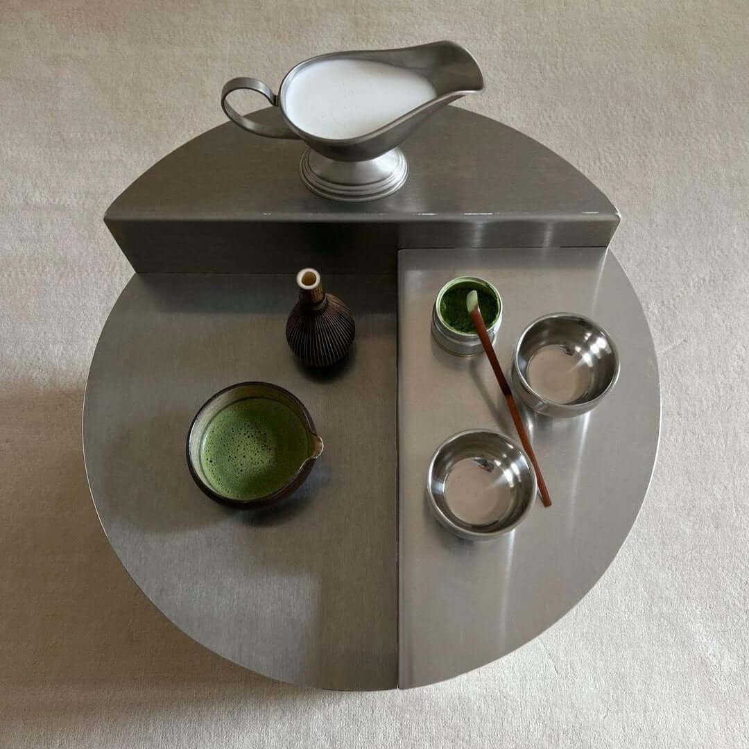 Elegant tea setup with cups and milk jug on a modern round tray, featuring a minimalist design and green tea presentation.