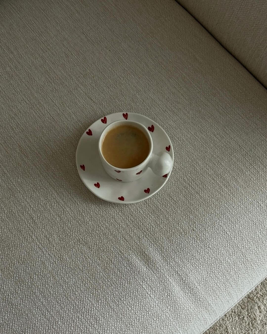 Ceramic mug with heart pattern and matching saucer on a textured surface.
