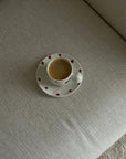 Ceramic mug with heart pattern and matching saucer on a textured surface.