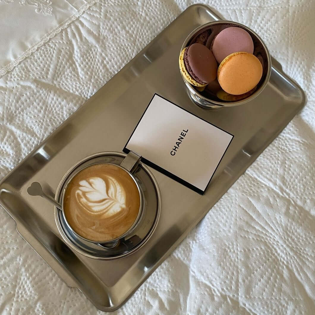 Stainless steel tray with coffee, macarons, and a branded card on a table.