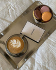 Stainless steel tray with coffee, macarons, and a branded card on a table.