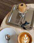 Urban Chic stainless steel serving tray with elegant dessert display, alongside a cup of cappuccino and a white saucer on a table.