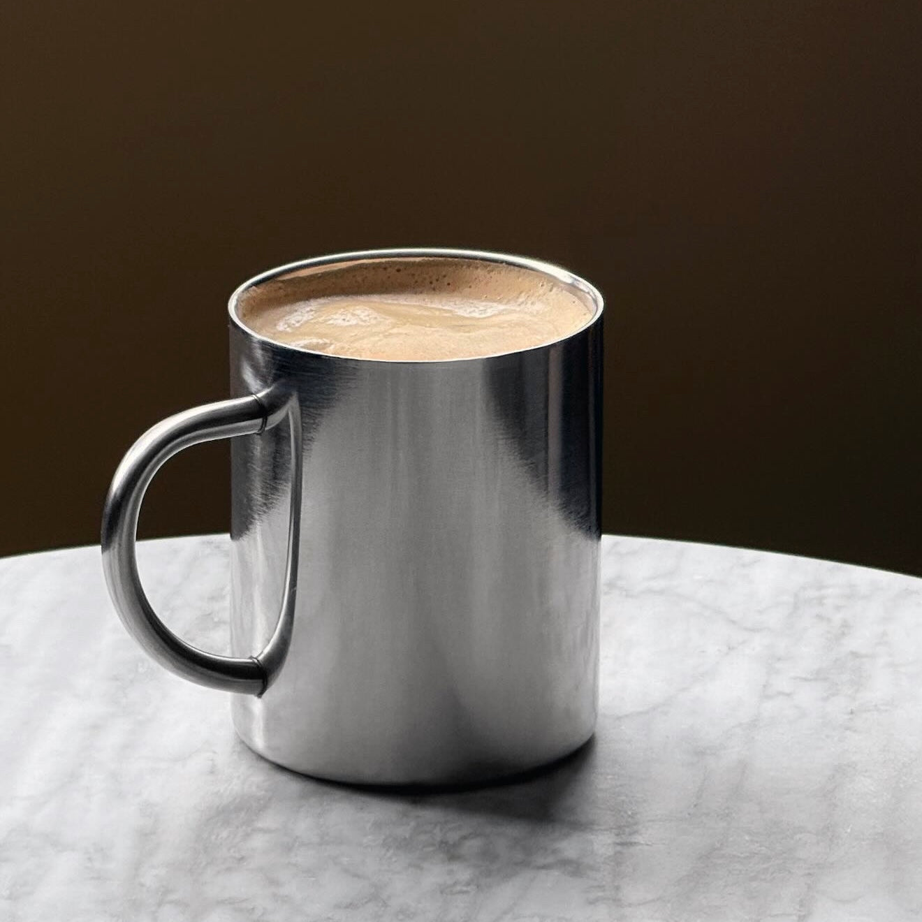 Sleek stainless steel coffee mug with frothy beverage on a marble table, part of the Aesthetic Stainless Bundle.