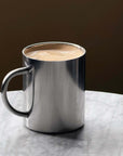 Sleek stainless steel coffee mug with frothy beverage on a marble table, part of the Aesthetic Stainless Bundle.
