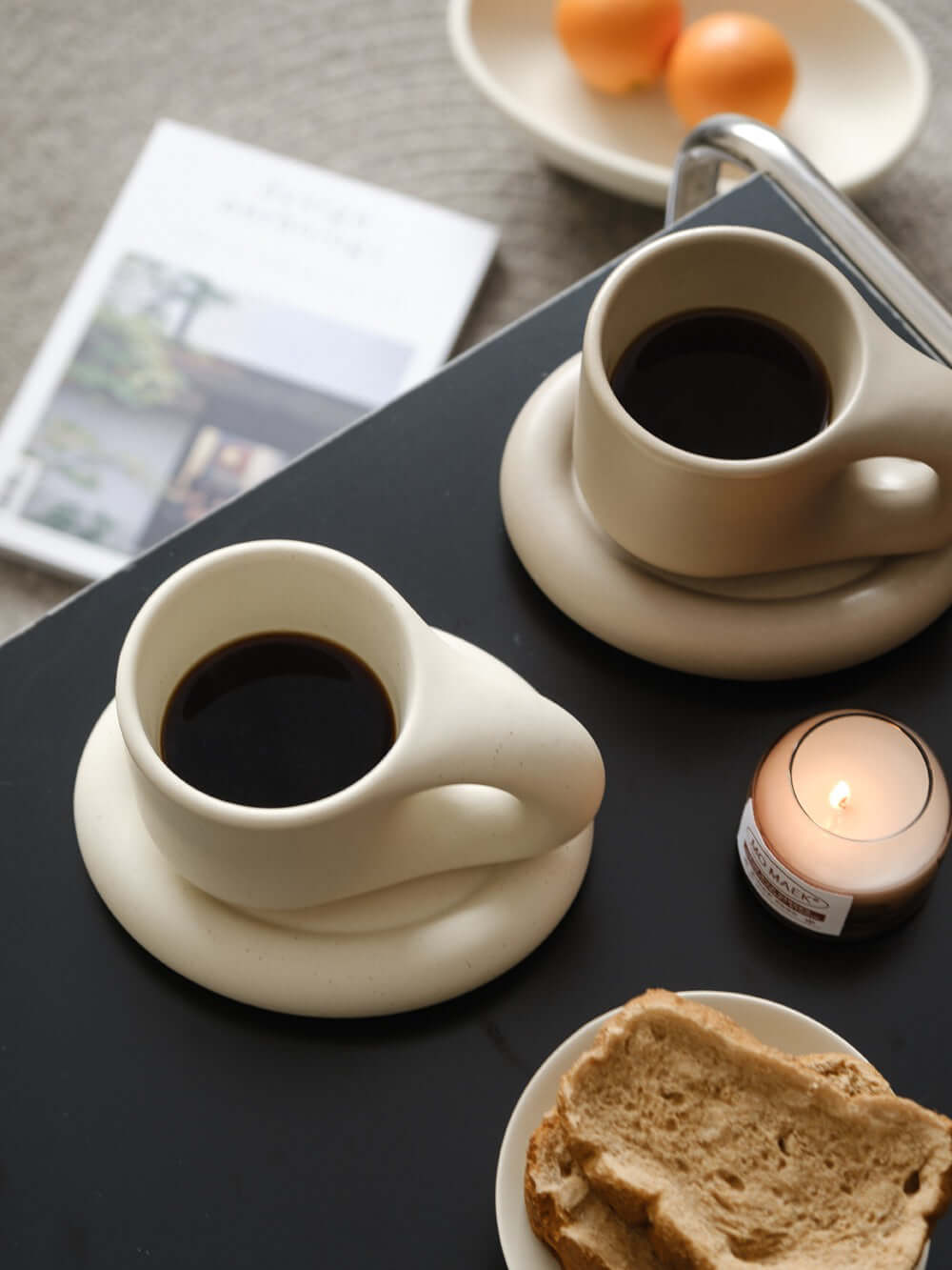 Minimalist Nordic chubby clay mug and plate set with coffee, bread, and candle on a stylish table setting.
