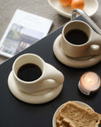 Minimalist Nordic chubby clay mug and plate set with coffee, bread, and candle on a stylish table setting.