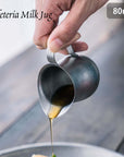 Hand pouring liquid from VINTAGE INOX 80ml stainless steel cafeteria milk jug.